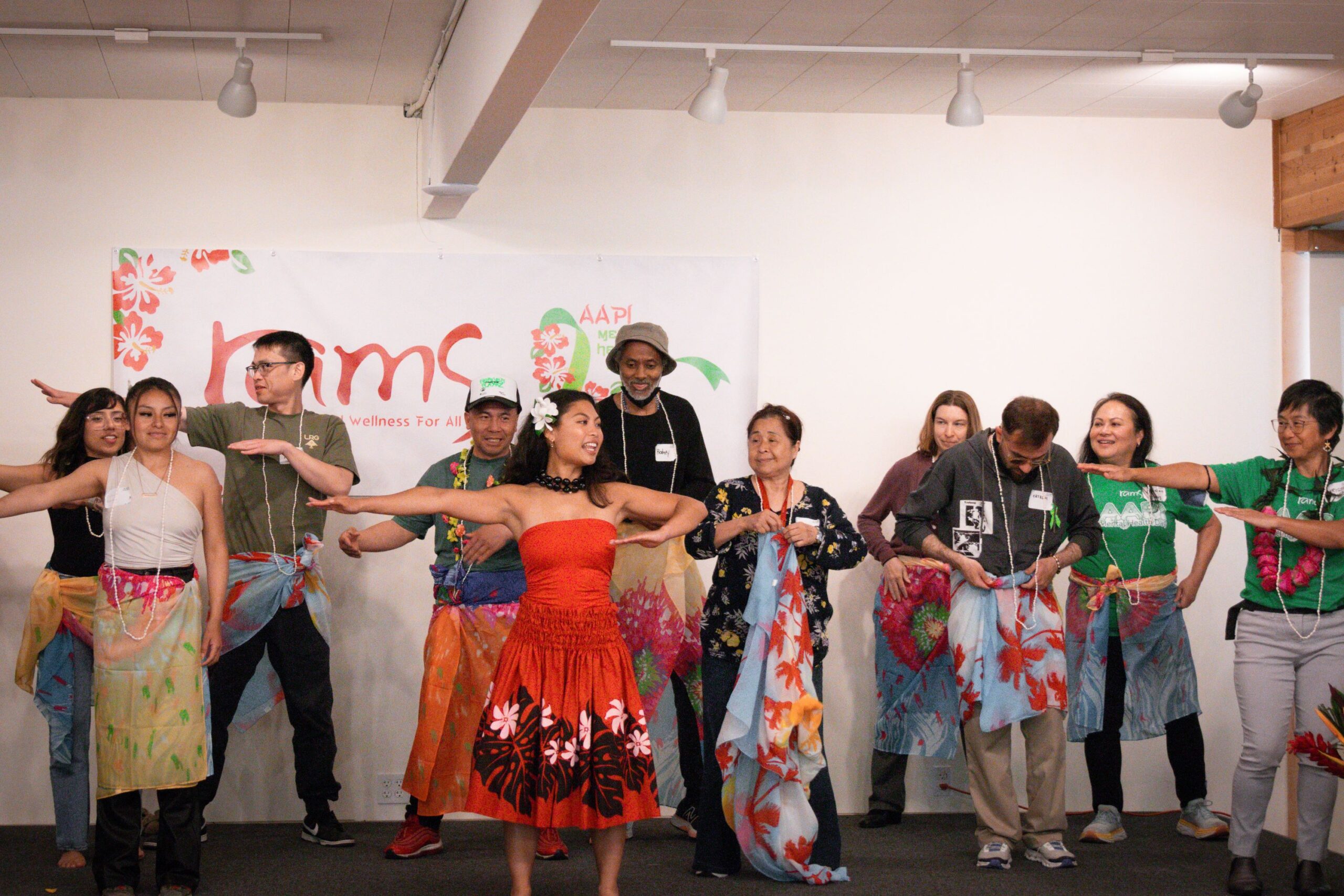 a group of meeting attendees participate in a hula dance on stage.