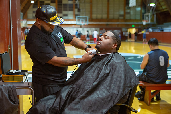 A Man getting a hair cut next to a basketball court