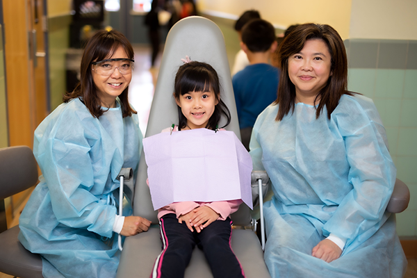 A kid getting a teeth check by 2 dentists